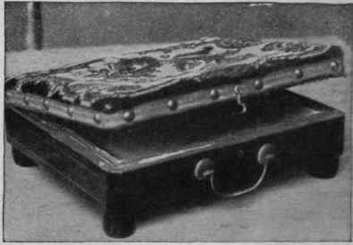 Footstool which holds a tin hot water fitment. The lid is of a single piece of carpet so that the heat is felt through. Placed beneath a bridge table or in a motor car such a footstool is a real comfort