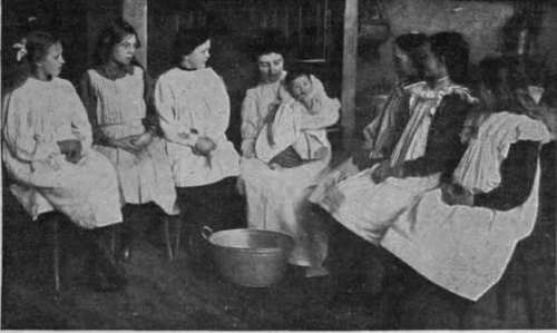 A class of little schoolgirls at Penarth. South Wales, learning how a baby should be bathed