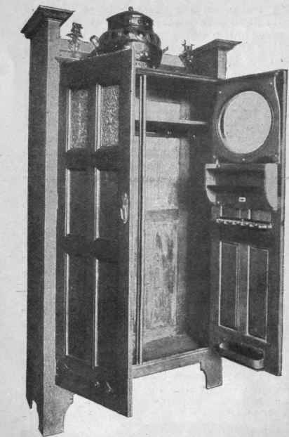 A hall wardrobe in fumed oak, fitted inside with umbrella stand, shelf, and hooks. The round mirror is a most useful adjunct