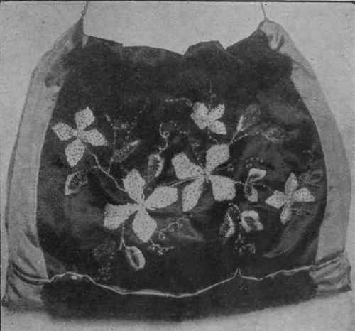 Black satin muff embroidered in clematis design. A dainty finish to the embroidery is given by sewing on scintillating beads in rose, white, and gold