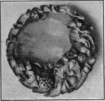 A circular brooch in gold tissue and tiny roses and leaves in the form of a wreath. This is one of the daintiest of floral brooches