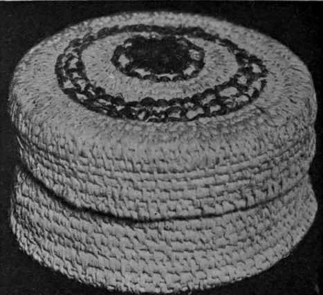 Raffia basket with cover. Decorated with a design in coloured raffia worked on the surface holding them in position, and working closely over them, as before.