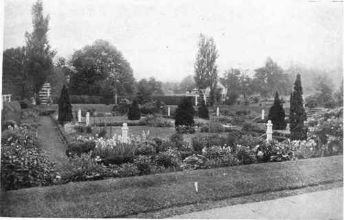 Fig. 126.   This shows the possibilities of making a picturesque garden on unpretentious lines. The beds are placed along the walks and the rectangular plats formed by the cross walks are left in turf. The Lombardy Poplars and conifers give a picturesque note to the scene, while the trees without, which are some distance from the enclosing hedge, form a pleasing setting.   See page 150.