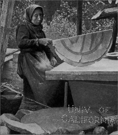 A NORWEGIAN WOMAN BAKING FLAT BREAD OUT OF DOORS.