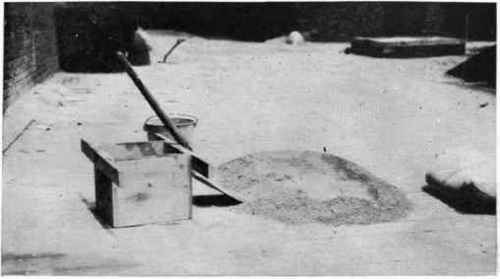 Sand and cement mixed ready to receive the water. A measuring box also is shown.