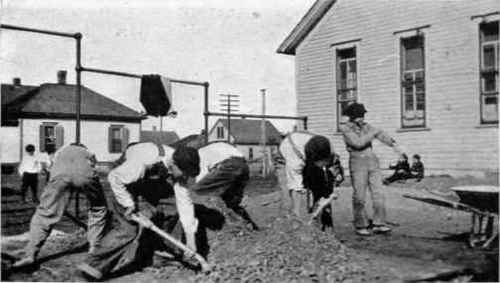 School boys mixing concrete preparatory to laying concrete sidewalk.